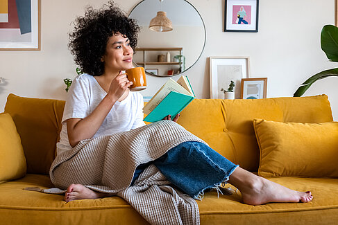 Gemütliches Wohnzimmer © iStock.com - Copyright Daniel de la Hoz Frau sitzt auf Sofa und trinkt Kaffee