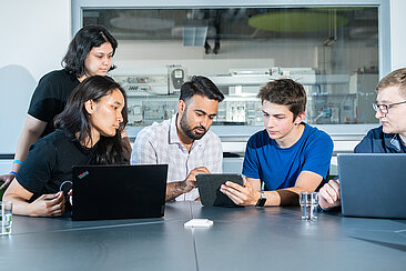 Studierende arbeiten zusammen an Tablet und Laptops